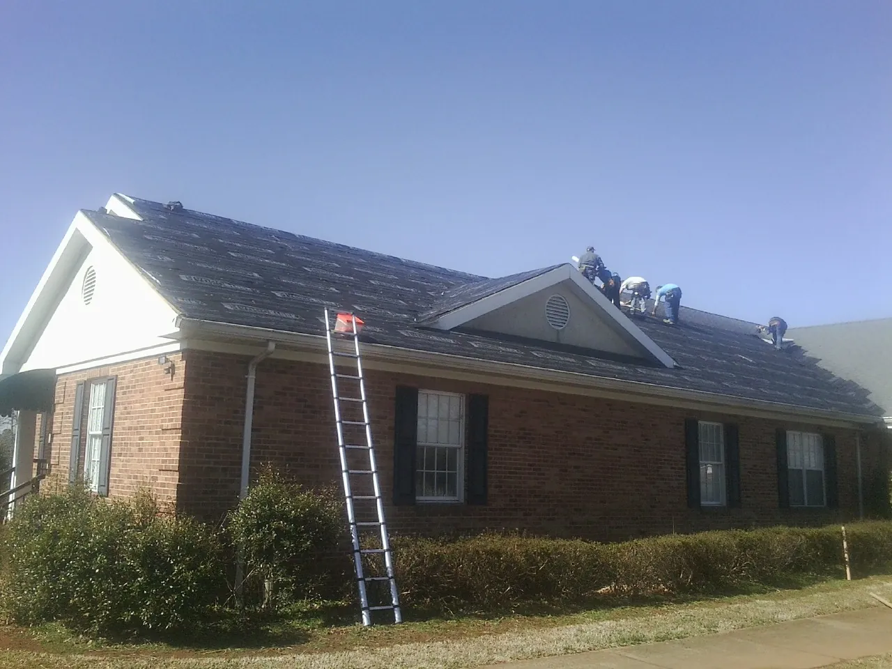 Crew tearing shingles off a brick ranch roof with a ladder set — Metal Roof Repair work by our crew in Wurtsboro