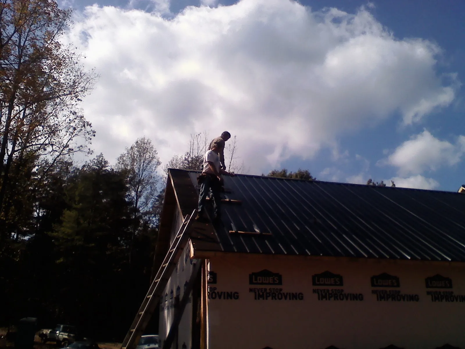 Roofer fastening dark metal panels high against a cloudy sky, from a Roof Inspection job in Wurtsboro