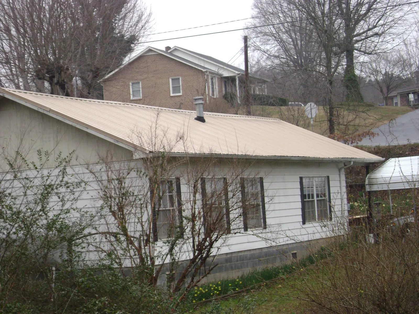Tan metal roof on a white sided house set into a hillside — Commercial Roofing by Roofing Brothers in Wurtsboro